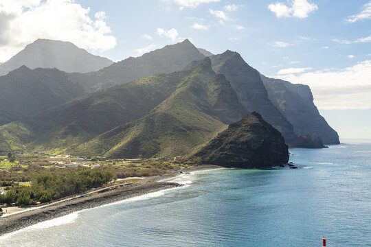 View of the rugged mountains and coastline of La Aldea de San Nicolas with a pebbled beach and turquoise ocean in Las Palmas de Gran Canaria, Canary Islands, Spain.