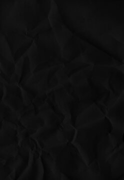 Close up of wrinkled black paper surface showing deep creases and shadows ideal for dark abstract backgrounds and grunge elements.