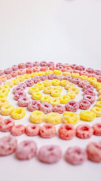 Colorful ring-shaped breakfast cereal in pink, yellow and orange arranged in a concentric spiral pattern on a white surface. Top view with copy space &mdash; perfect for breakfast, food, creativity and patt