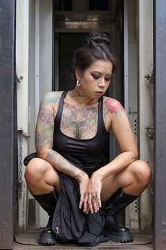 Tattooed Asian woman crouches in the doorway of a train carriage