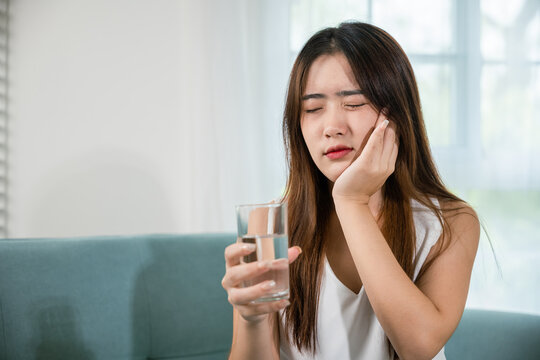Asian young woman with sensitive teeth holding glass of cold water