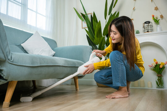 Happy Asian young woman with accumulator vacuum cleaner at home in living room
