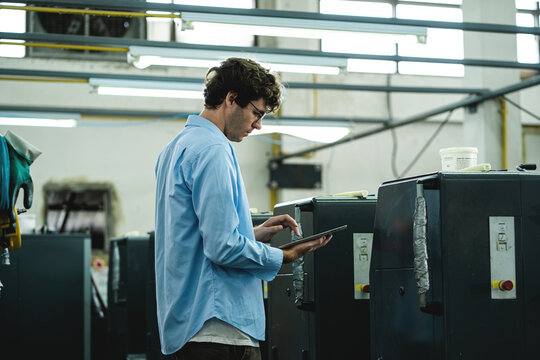 Printing Factory Employee Using a Tablet to Monitor Production Information and Manage Commercial Printing Operations Inside an Industrial Facility.  