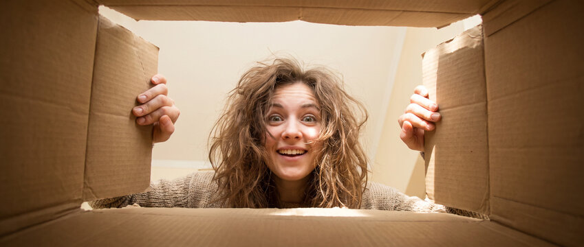excited young woman opening cardboard box and smiling at camera, unboxing surprise package at home, ecommerce delivery concept, joyful reaction, lifestyle shopping, happy customer happiness experience