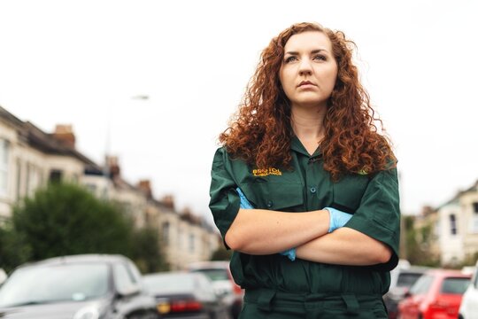 Person in green uniform stands confidently on a street with arms crossed.