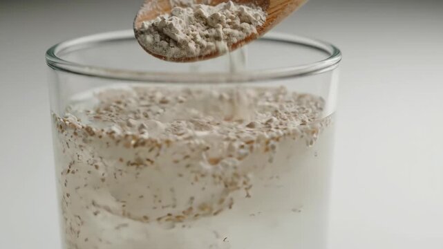 Oat husk sprinkled into glass of milk with wooden spoon creating nutritious breakfast and powdered husk mixed in glass for healthy hydration