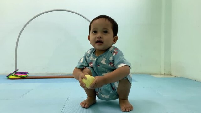 Happy toddler playing with a tactile ball, sitting on a blue floor, real-time video clip