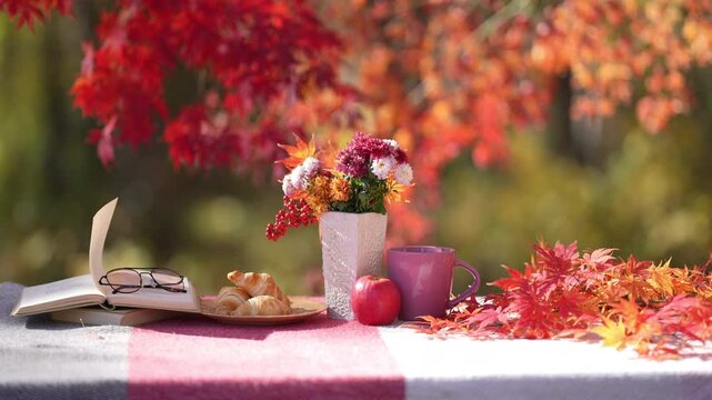 Cozy autumn breakfast with open book, croissants, apple, flowers and mug outdoors. Cozy fall reading with hot drink. Autumn with open book. Cozy autumn fall. Reading with coffee during autumn morning.