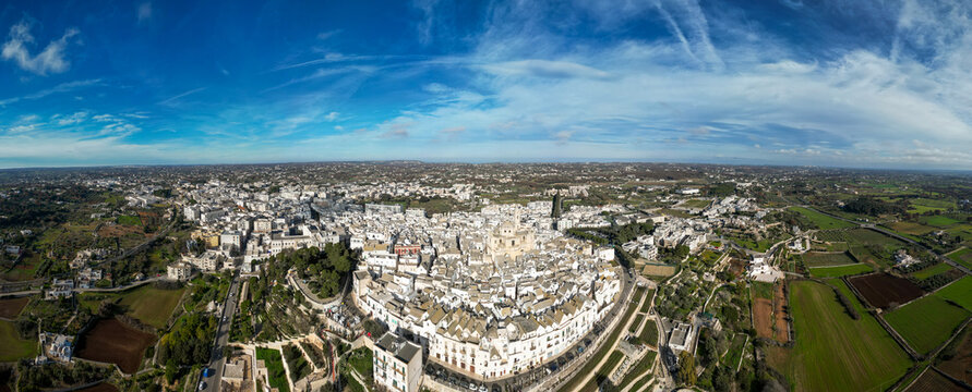 Aerial view of the historic white town of Locorotondo with its dense cluster of buildings, church dome, and surrounding agricultural fields in Locorotondo, Apulia, Italy.