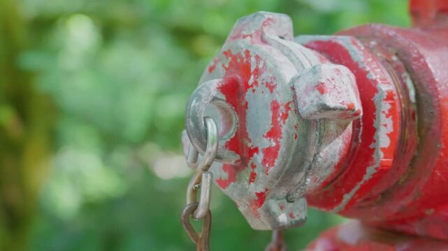 Macro close up of weathered red fire hydrant valve nozzle cap with metal safety chain