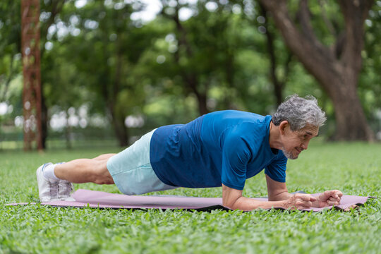 active senior asian man doing elbow plank exercise on yoga mat in green public park