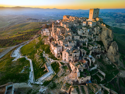 Aerial view of the historic abandoned ghost town of Craco perched on a rocky hilltop surrounded by rolling hills at golden hour in Craco, Basilicata, Italy.
