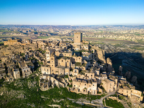 Aerial view of the abandoned ghost town of Craco, featuring historic stone buildings, a prominent tower, and rugged landscape in Craco, Basilicata, Italy.