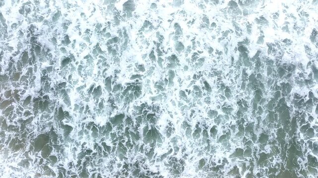 Aerial surf with white foam. Drone view of sea foam movement. Foamy shoreline from above. Ocean foam flowing toward beach. Drone captures rolling foamy waves.