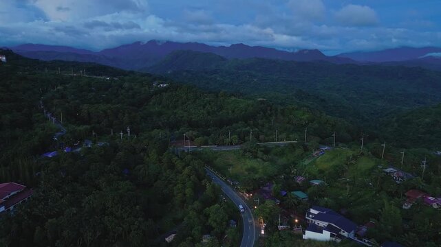 High altitude aerial footage showcasing illuminated caf&eacute;s, winding mountain roads, dense tropical forests, and expansive rolling hills along Marcos Highway in Tanay, Rizal, Philippines.
