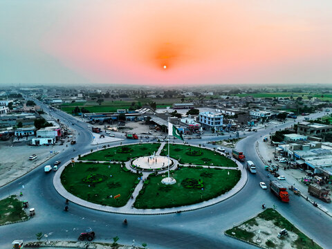 Aerial view of Pakistan Chowk featuring a fighter jet monument and the Pakistani flag in a central roundabout during sunset in Dera Ghazi Khan, Punjab, Pakistan.