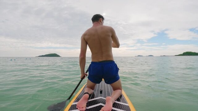 Caucasian young man rows on a paddleboard as glides over the ocean waves. 