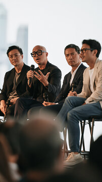 Panel Discussion: Four men sit on a stage, with one speaking into a microphone, engaged in a panel discussion. Their attentive expressions suggest a thoughtful exchange of ideas.