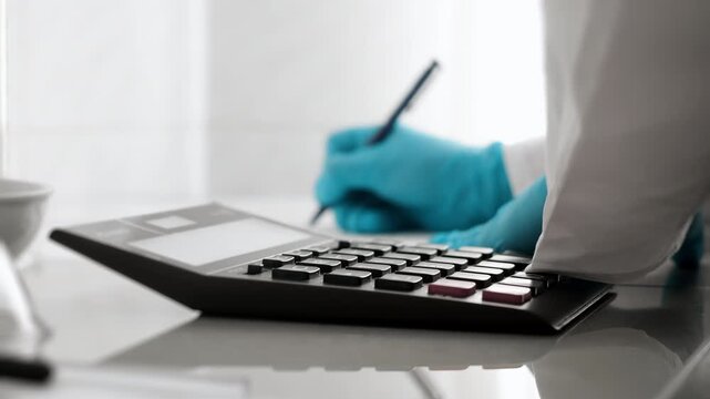 Laboratory specialist calculates data on a calculator and records results in documents during scientific testing, analysis and quality control.