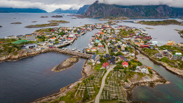 Aerial view of the fishing village of Henningsvaer with its colorful houses, harbor, and traditional fish drying racks surrounded by rocky islands and mountains in Henningsvaer, Nordland, Norway.