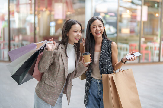 Two happy Asian women carrying shopping bags for Black Friday sale promotion