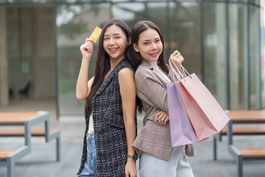 Two Asian women holding shopping bags and credit card outdoors for Black Friday sale promotion