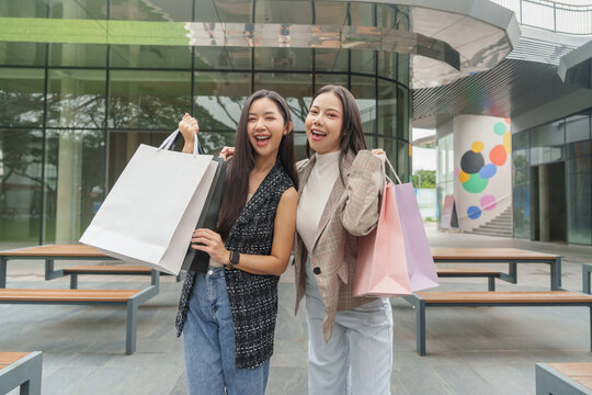Happy Asian women showing paper bags during Black Friday retail shopping sale