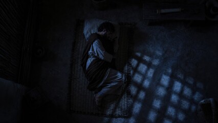 Obraz premium Joseph sleeping in a dark room. Biblical scene depicting man resting on a mat during the divine vision. Religious concept of the nativity story, faith, and spiritual guidance at Christmas.