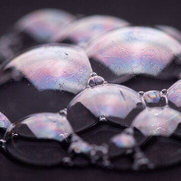 Iridescent soap bubble film floating above black surface in ethereal glow