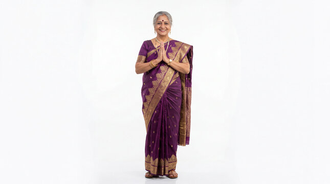 Senior indian woman in purple sari with gold border smiling and greeting with namaste hands cultural respect and hospitality concept