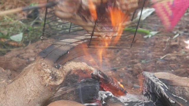 A whole chicken is being grilled using iron tongs over a traditional wood fired stove.
