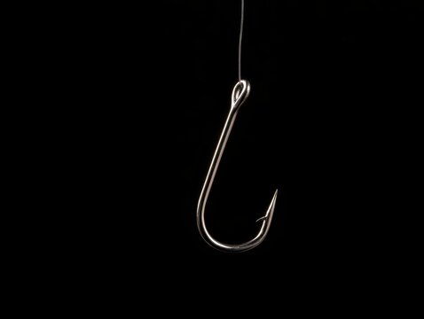 A sharp metal fishing hook hanging from a thin fishing line against a solid black background