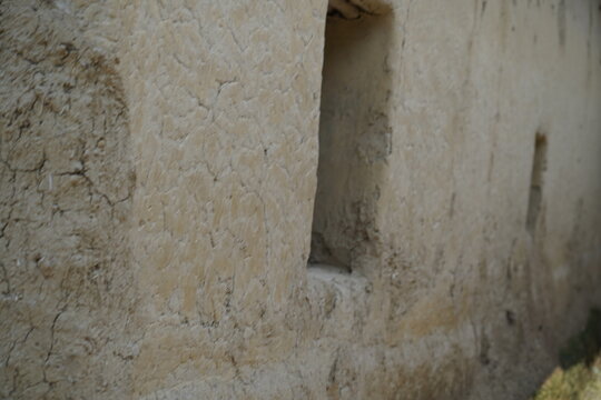 An old weathered wall made of mud bricks with a narrow vertical opening in a rural setting