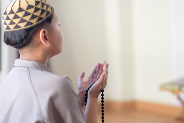 Side profile portrait of sincere young Muslim boy wearing traditional kufi cap performing faithful supplication with prayer beads during peaceful spiritual devotion © Kornkanok