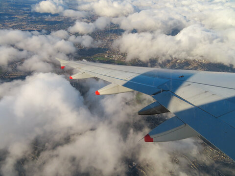 Aerial view of an airplane wing flying above the clouds with the urban landscape of London visible below in London, England, United Kingdom.