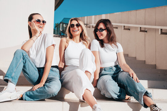 Three young beautiful smiling hipster female in trendy summer white t-shirt  and jeans clothes. Sexy carefree women posing in street. Positive models having fun, going crazy. In sunny day, sunglasses