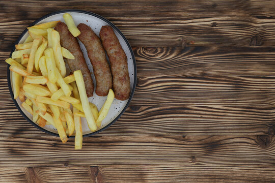 Grilled kebapche sausages with french fries on a plate over a dark wooden table background top view