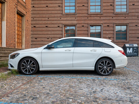 White Mercedes Benz CLA Shooting Brake parked on cobblestones in front of Museo del Violino in Cremona, Italy