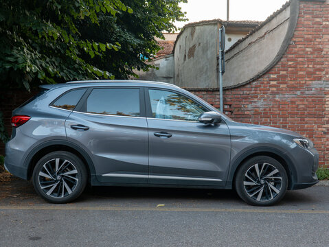 MG HS SUV in grey color parked on a street by a brick wall and green trees, modern urban automobile design