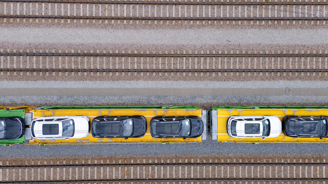 Aerial view of a freight train transporting new cars on flatbed rail cars along parallel train tracks in Gdansk, Poland.