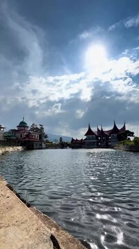 Traditional Minangkabau rumah gadang house and mosque standing beside rippling reservoir water, cinematic video representing Indonesian cultural architecture, tranquil lake scenery and West Sumatra he