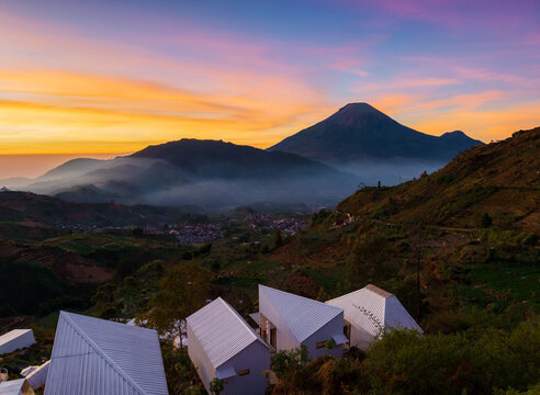 Aerial view of Sikapuk Hill and Villa Dieng featuring modern white villas nestled in a lush mountain landscape under a vibrant sunset sky in Indonesia.