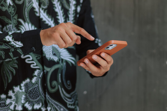 Close up side view of man in batik shirt tapping smartphone screen, embodying heritage workflow, seamless mobile engagement, and cultural fintech solutions