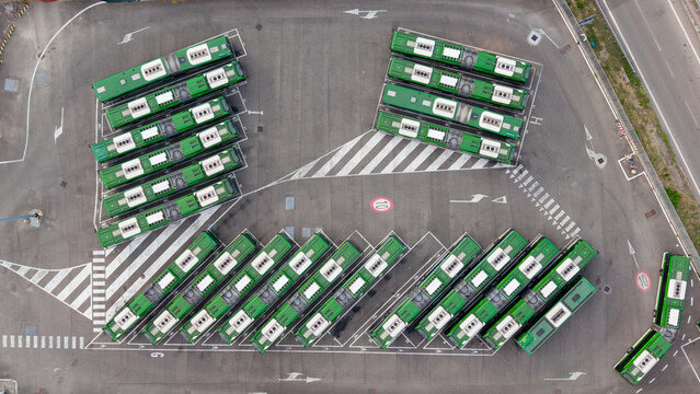 Aerial view of an electric bus depot with rows of green buses parked on asphalt in Milan, Lombardy, Italy.