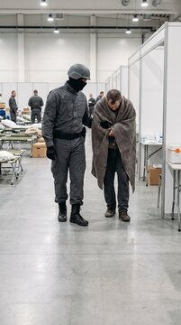 Soldier in uniform escorting a refugee wrapped in a blanket in a shelter