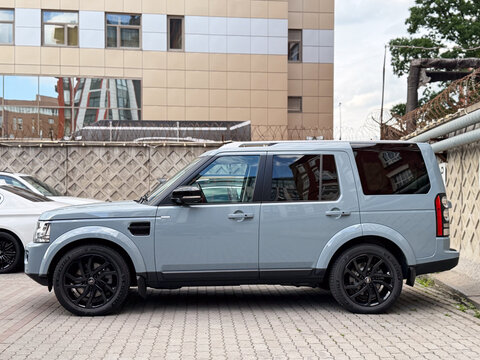 Land Rover Discovery 4 luxury SUV wrapped in Nardo Grey polyurethane vinyl film, parked on a city street pavement. Premium British 4x4 off-road vehicle with custom glossy paint protection wrap. 