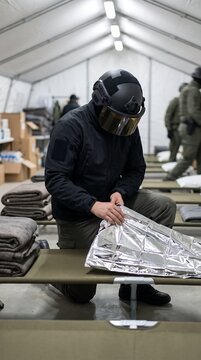 Military or emergency response personnel setting up foil thermal blanket on cot in shelter tent