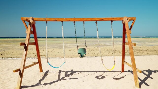 An empty swing on a sandy beach at low tide. The desert atmosphere at sea. The concept of tourism and travel.