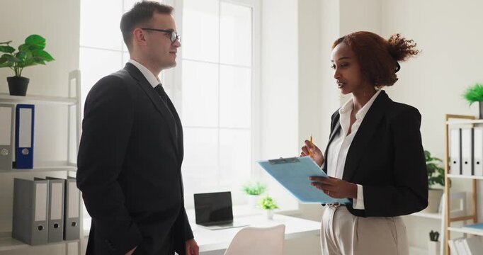 Business professionals in office discussion with clipboard. Two coworkers review a report, aligning next steps. Natural light enhances focus. Bright modern office conveys trust and clarity.