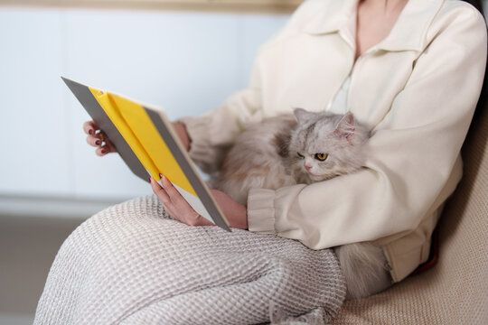 Cropped shot of woman reading book with cat sitting on lap at home